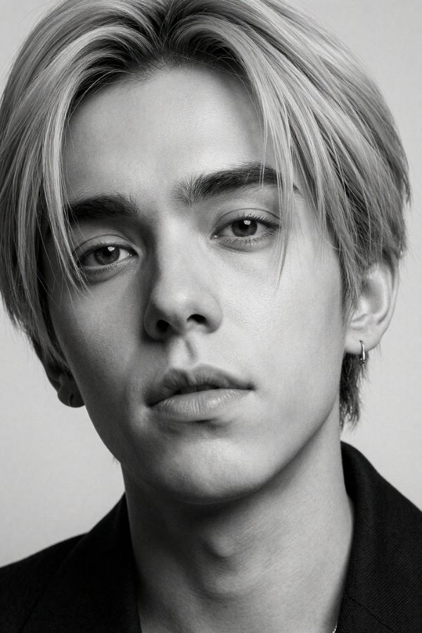 Black and white close-up portrait of a young man with layered, light-toned hair, wearing a dark collared shirt, gazing directly at the camera with a neutral expression.