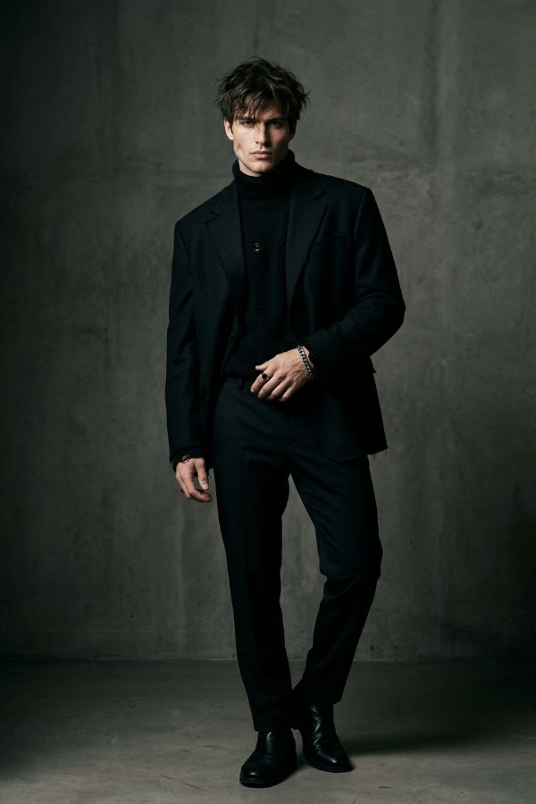 A cool male model with strong jawline, messy hair, black outfit, studio lighting, minimal background, high fashion photography